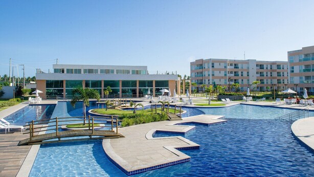 A large outdoor swimming pool with multiple sections and a modern building in the background.