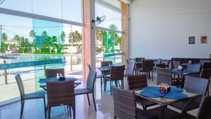 A restaurant with outdoor seating overlooking a pool and palm trees.