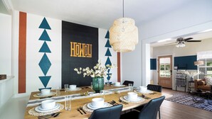 A dining area with a wooden table set for four, surrounded by chairs. A decorative wall with geometric patterns and the word "HOWL" is visible.