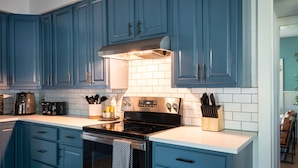 A kitchen with blue cabinets, a black stove, and white tiles.