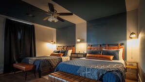 A modern bedroom with two beds, a ceiling fan, bedside lamps, and a bench.