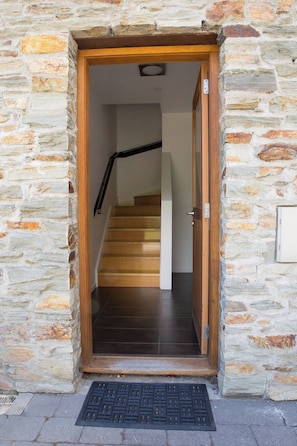 Enter through the stone entrance to a grand staircase with a dark wooden staircase and black handrail.