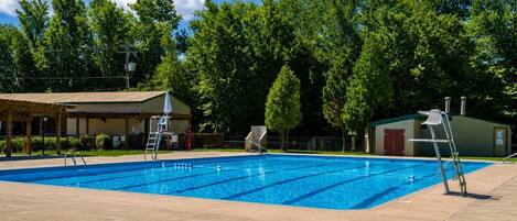 Una piscina con una silla de salvavidas, una zona de estar cubierta y un pequeño edificio al fondo.