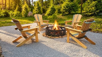 Un foyer entouré de quatre chaises Adirondack, installé sur une surface de gravier, avec une terrasse en bois et de la verdure en arrière-plan.