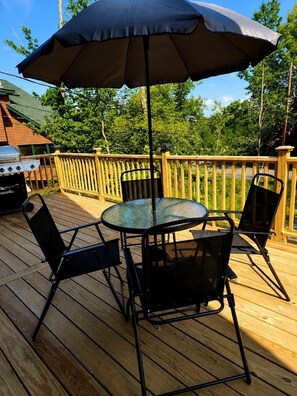 A wooden deck with a round glass table and four chairs, an umbrella, and a grill. - New Arcades Game Room, Firepit, Pet Friendly (Hamlin)