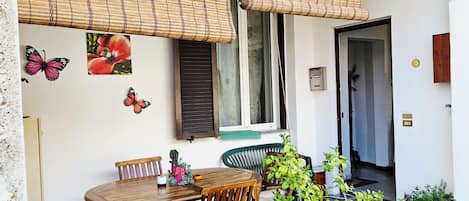 A patio with a wooden table and chairs, a hanging bamboo blind, and potted plants.