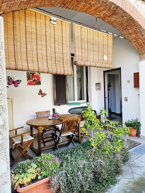 A patio with a wooden table and chairs, a hanging bamboo blind, and potted plants.