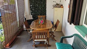 Un patio con un tavolo rotondo in legno e sedie, una panca imbottita verde e un cactus, oltre a una parete decorativa.