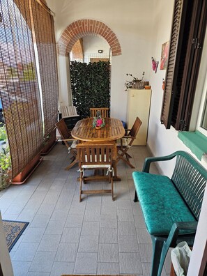Un patio con un tavolo rotondo in legno e sedie, una panca imbottita verde e un cactus, oltre a una parete decorativa.