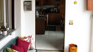 A room with a green chair, a wooden bench, a welcome mat, and a view into a kitchen area with wooden cabinets and a microwave. - LaCasaDeiNonni - Lakes&Relax (Varano Borghi)