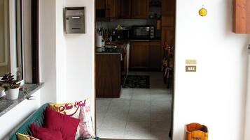 Una stanza con una sedia verde, una panca di legno, un tappetino d'ingresso e vista su un angolo cottura con pensili in legno e un forno a microonde.