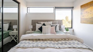 A modern bedroom with a large bed, two bedside tables, a window, and a painting on the wall. - Stunning, modern, two-story detached townhouse (Footscray)