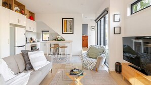 A modern living room with a sofa, coffee table, TV, and a kitchen area in the background. - Stunning, modern, two-story detached townhouse (Footscray)