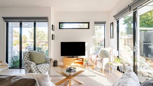 A modern living room with a flat-screen TV, comfortable seating, and large windows offering a view of the outdoors. - Stunning, modern, two-story detached townhouse (Footscray)