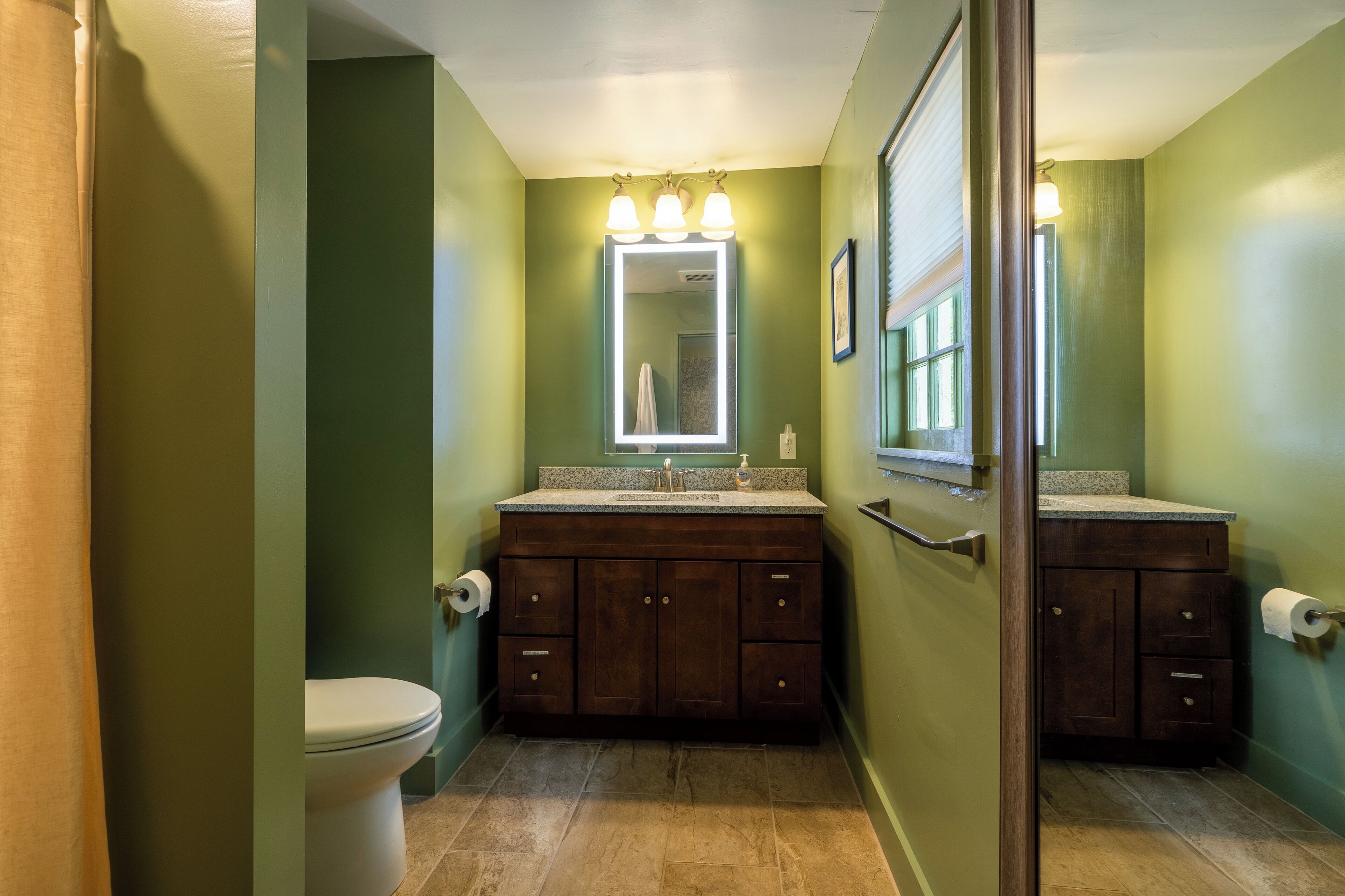 A bathroom with a toilet, a sink with a mirror, and a shower area.