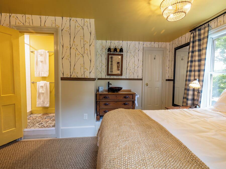 Une chambre à coucher avec un lit, une commode, un miroir et une fenêtre avec des rideaux.