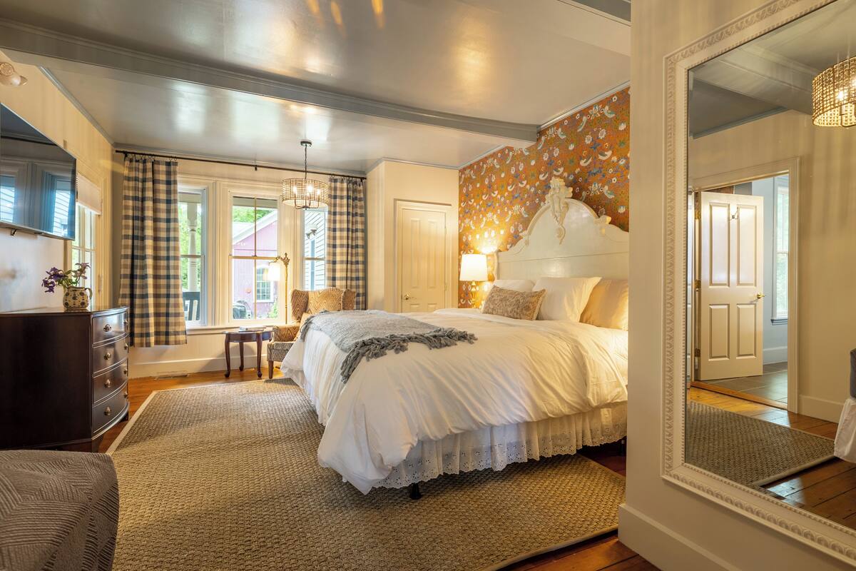 A bedroom with a large bed, a dresser, a chair, and a mirror.