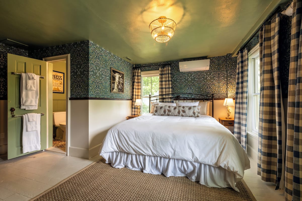 A bedroom with a large bed, a green door, and a window with curtains.
