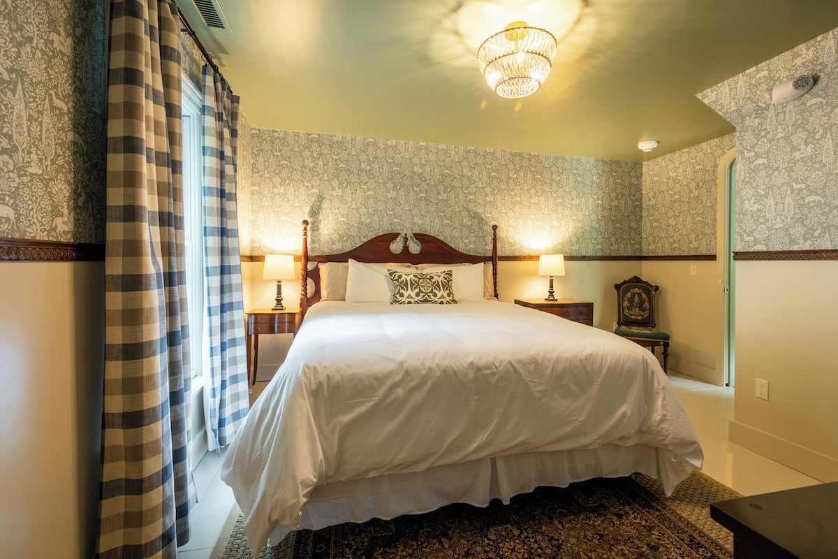 A neatly made bed with a wooden headboard, two bedside lamps, and a patterned wall.