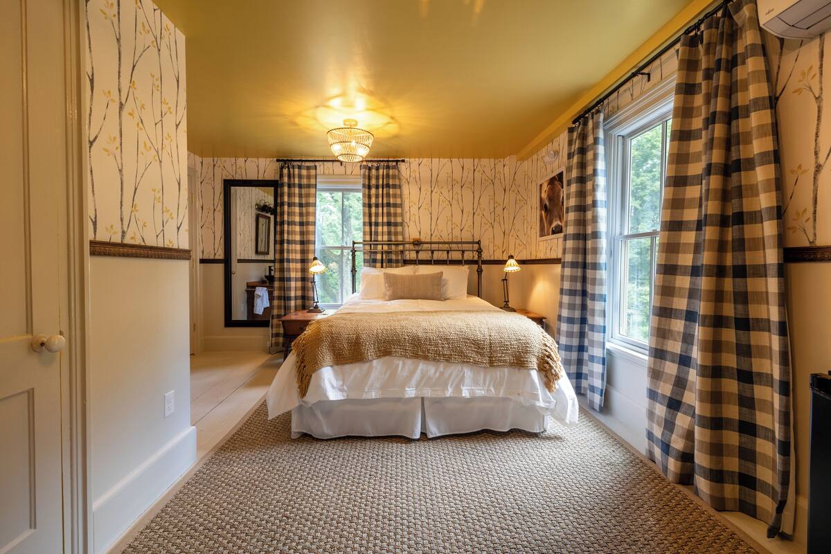 A bedroom with a large bed, a chandelier, and checkered curtains.