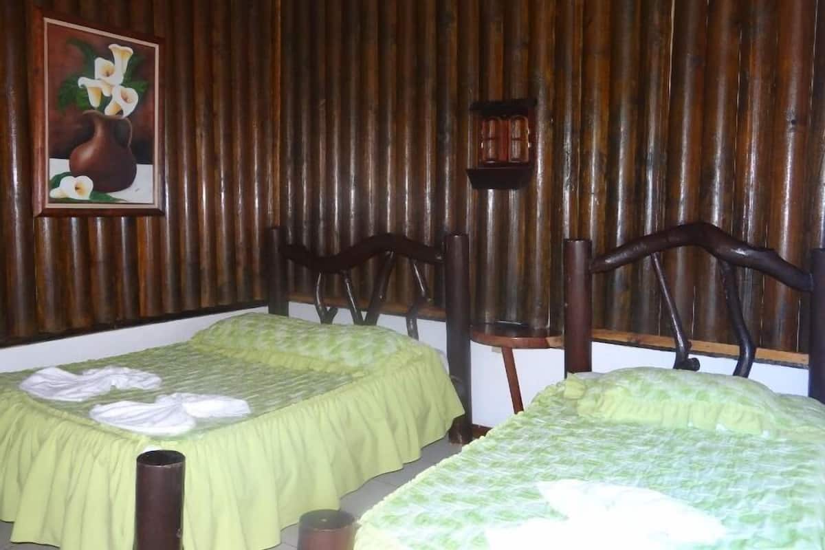 A room with two beds, wooden walls, a painting of flowers, and a small table.
