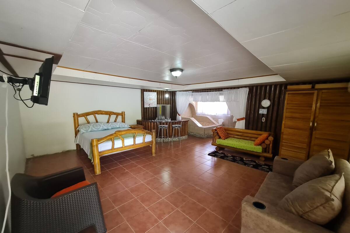 A spacious room with a bed, a sofa, a small table, and a chair.