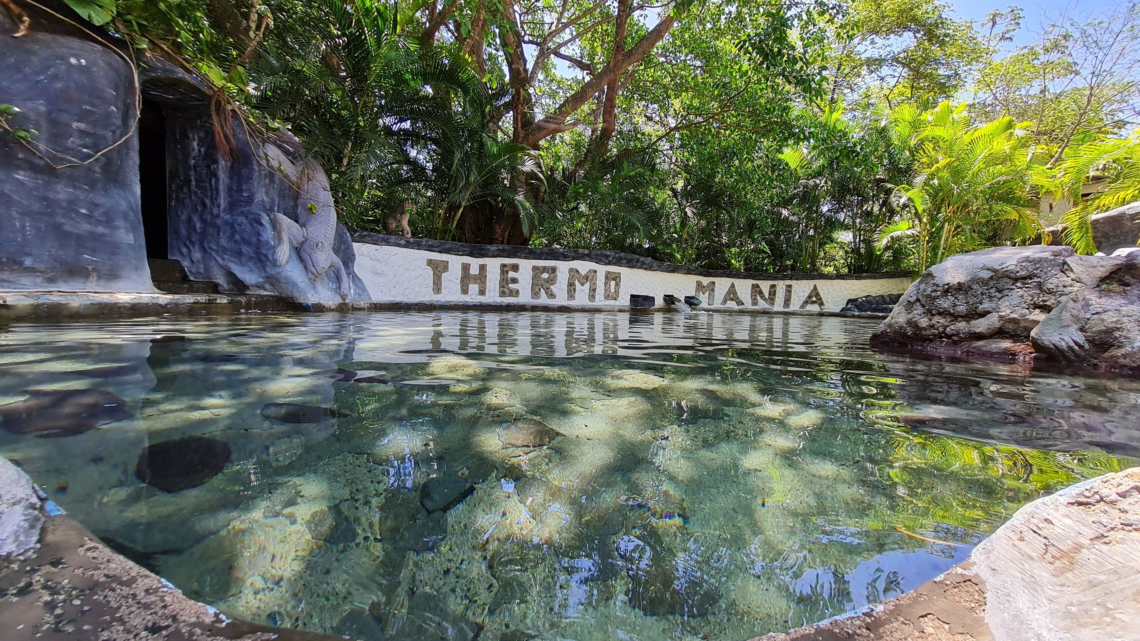 A clear pool with rocks and a wall with the words "THERMO MANIA" visible.