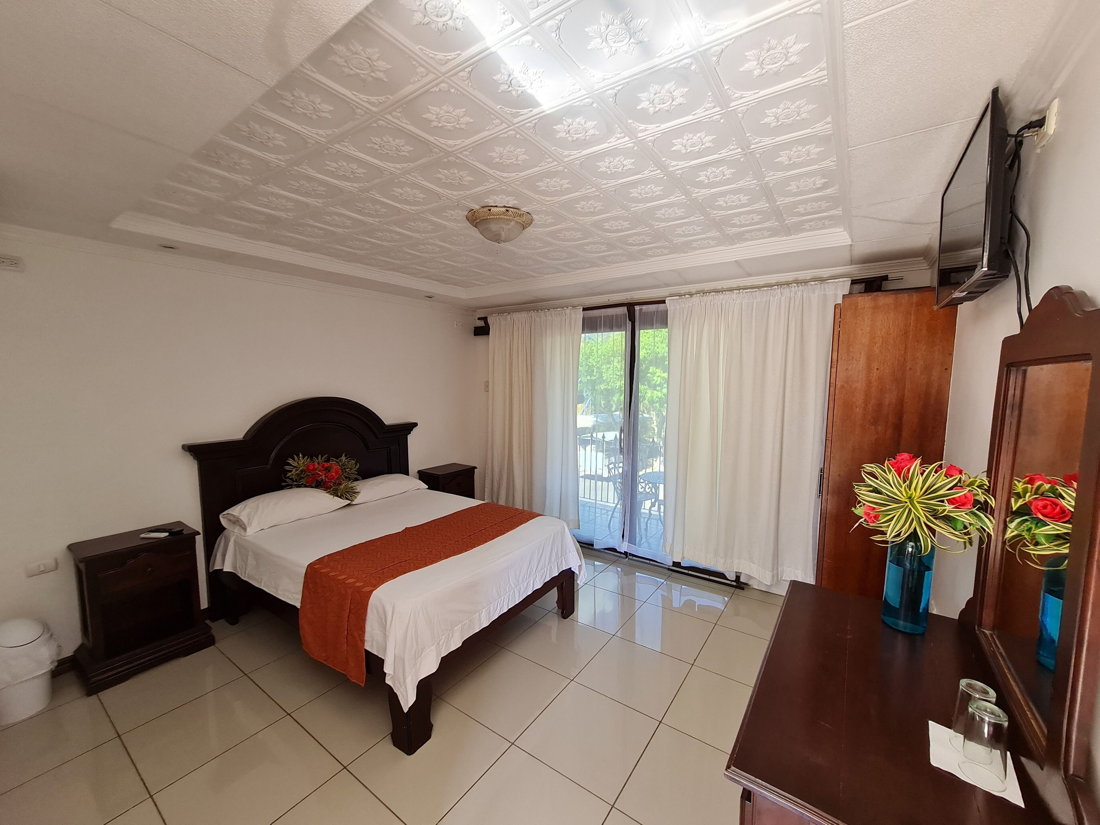 Habitación de hotel con una cama grande, un aparador de madera, un espejo y un techo con motivos florales.
