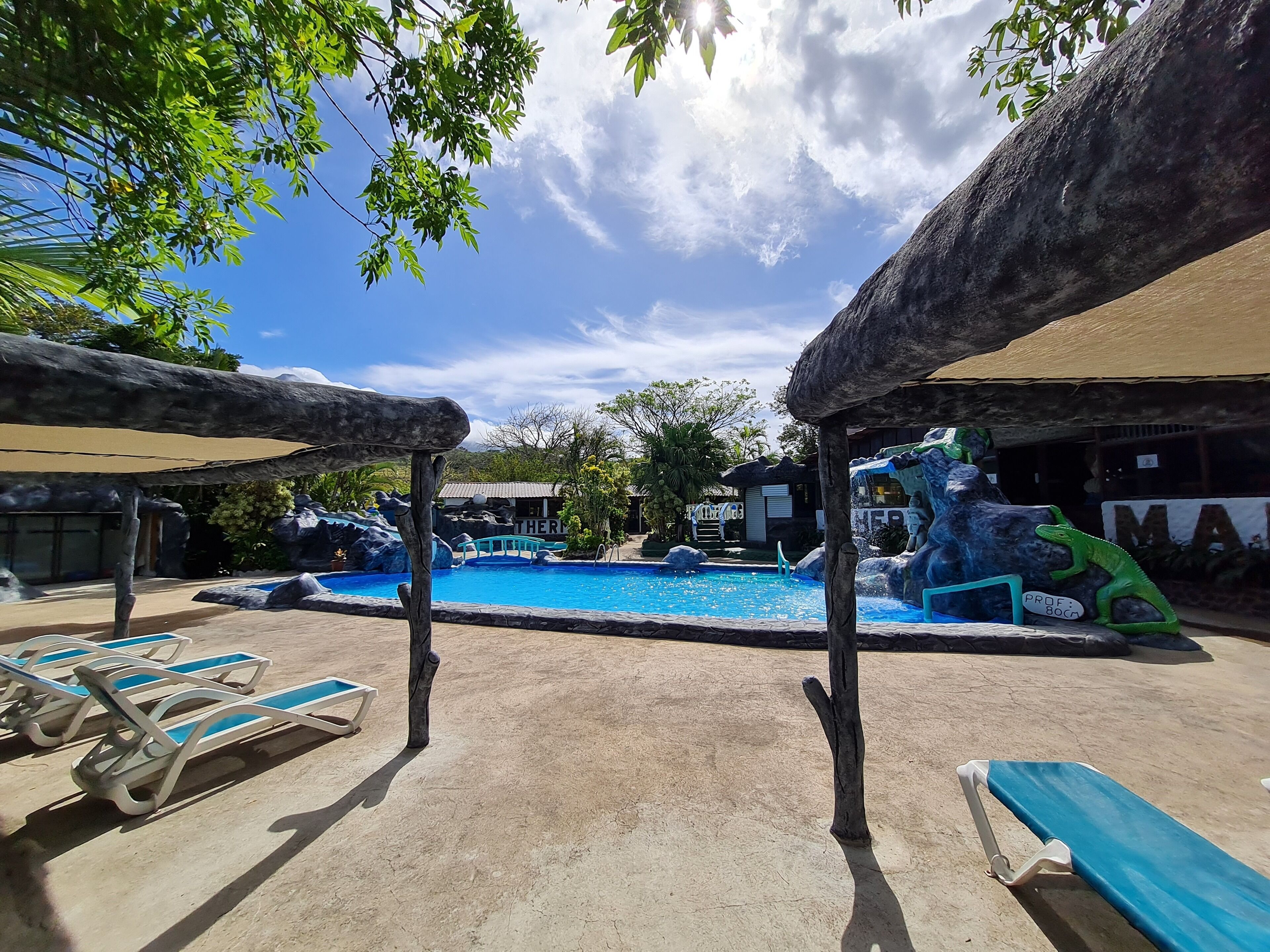 A pool area with lounge chairs, a water slide, and a thatched-roof structure.