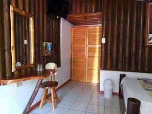A room with a wooden desk, a chair, a bed, a television, and a door. - Thermomania (Fortuna)