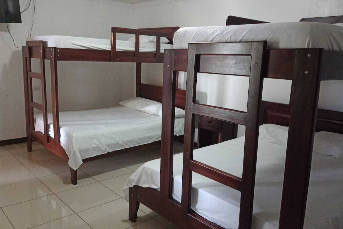 A room with three wooden bunk beds, white bedding, and a tiled floor.