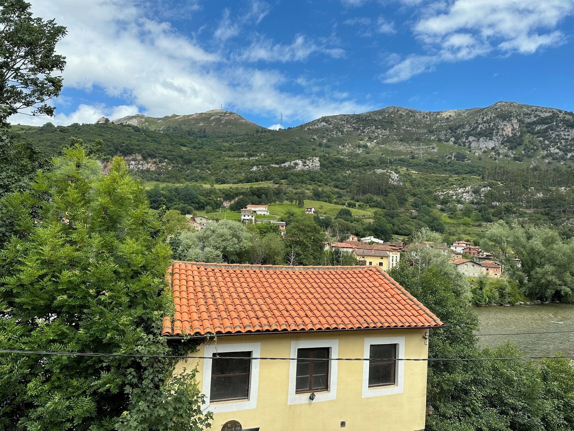 Un edifici groc amb teulada de rajoles vermelles, envoltat de vegetació abundant i un riu.