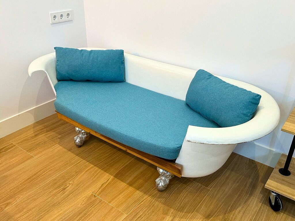 A white bathtub with a blue seat and two pillows, placed on a wooden floor with a white wall in the background.