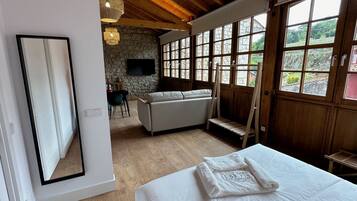 Een slaapkamer met een groot bed, een stenen muur, een houten plafond en een televisie op de achtergrond.