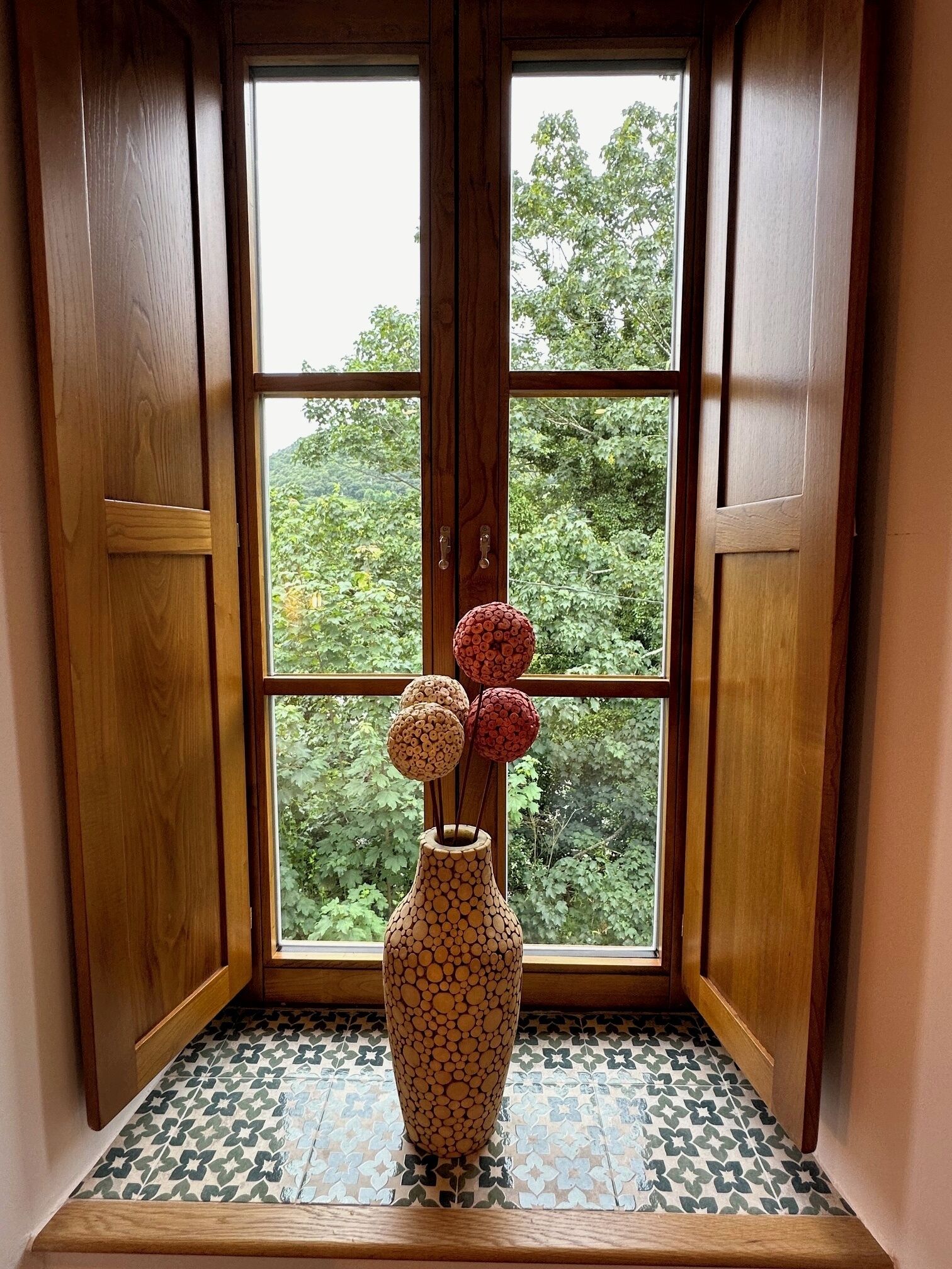Una puerta de madera con un ventanal, un jarrón estampado con decoraciones esféricas y un suelo de baldosas.