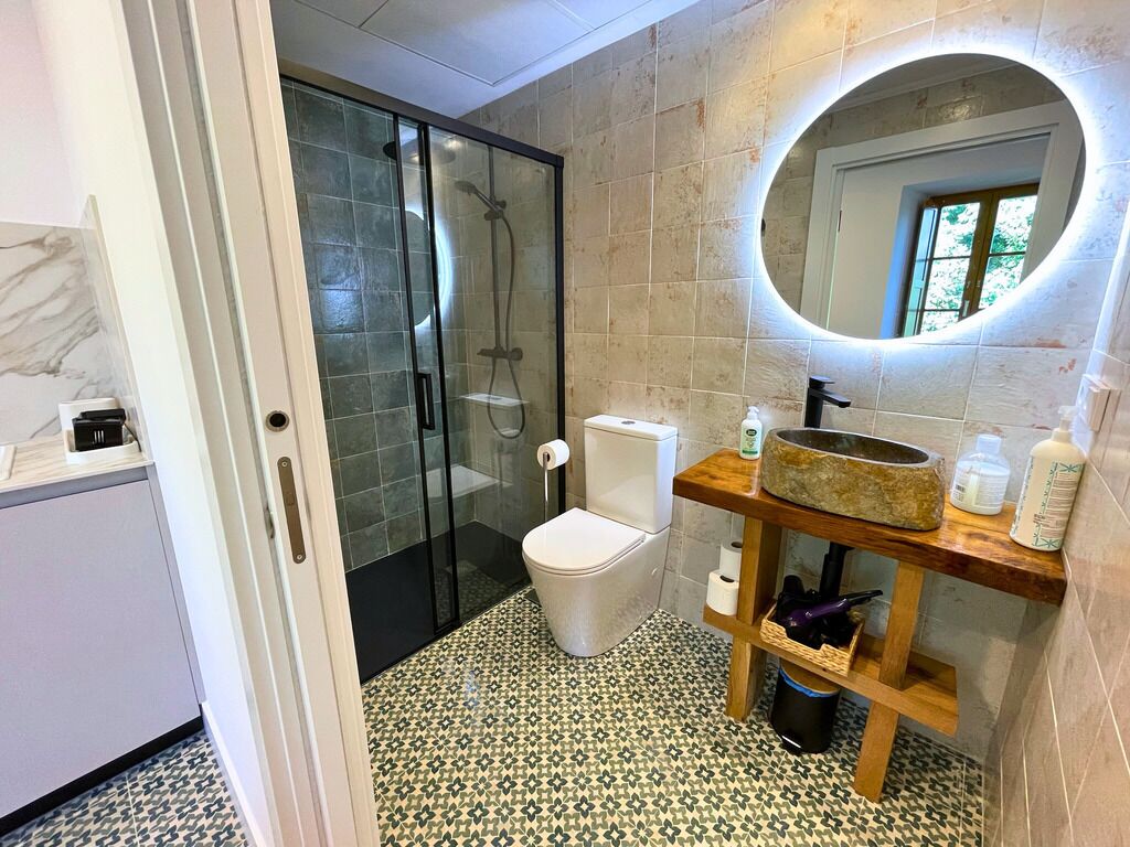 Een badkamer met een glazen douchecabine, toilet, wastafel met een marmeren blad en een spiegel met een ronde lijst.