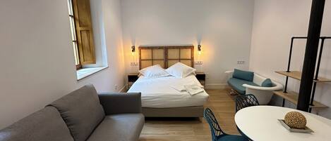 Una habitación de hotel moderna con una cama grande, un sofá, una mesa de comedor y una pequeña cocina.