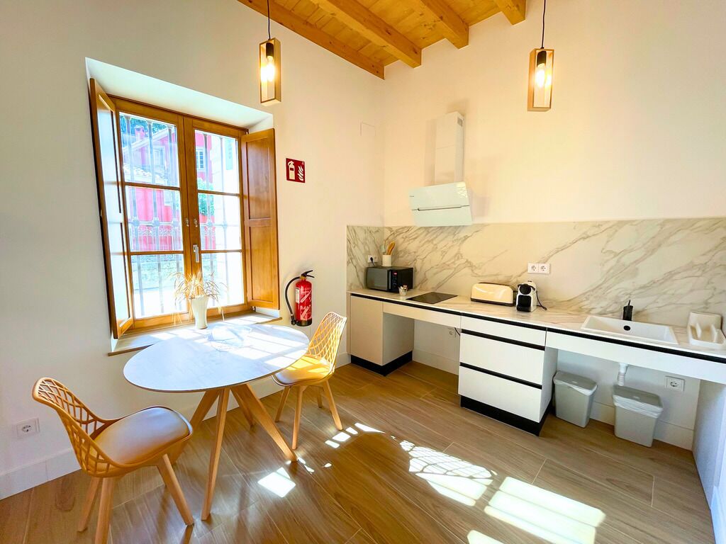 Una cucina moderna con un tavolo da pranzo rotondo, sedie di legno, un piano di lavoro bianco e una parete rivestita in marmo.