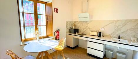Una cocina moderna con una mesa redonda, sillas de madera, encimera blanca y salpicadero de mármol.