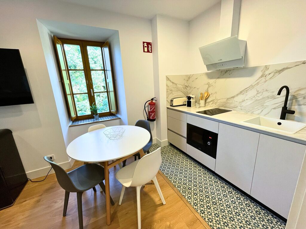 Une cuisine compacte avec un plan de travail blanc, un évier et une fenêtre donnant sur un espace verdoyant.