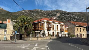 Un edificio con tejado de tejas rojas y ventanas amplias, rodeado de un muro de piedra y una palmera.