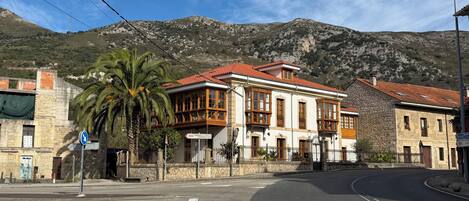A building with a red-tiled roof and large windows, surrounded by a stone wall and a palm tree.