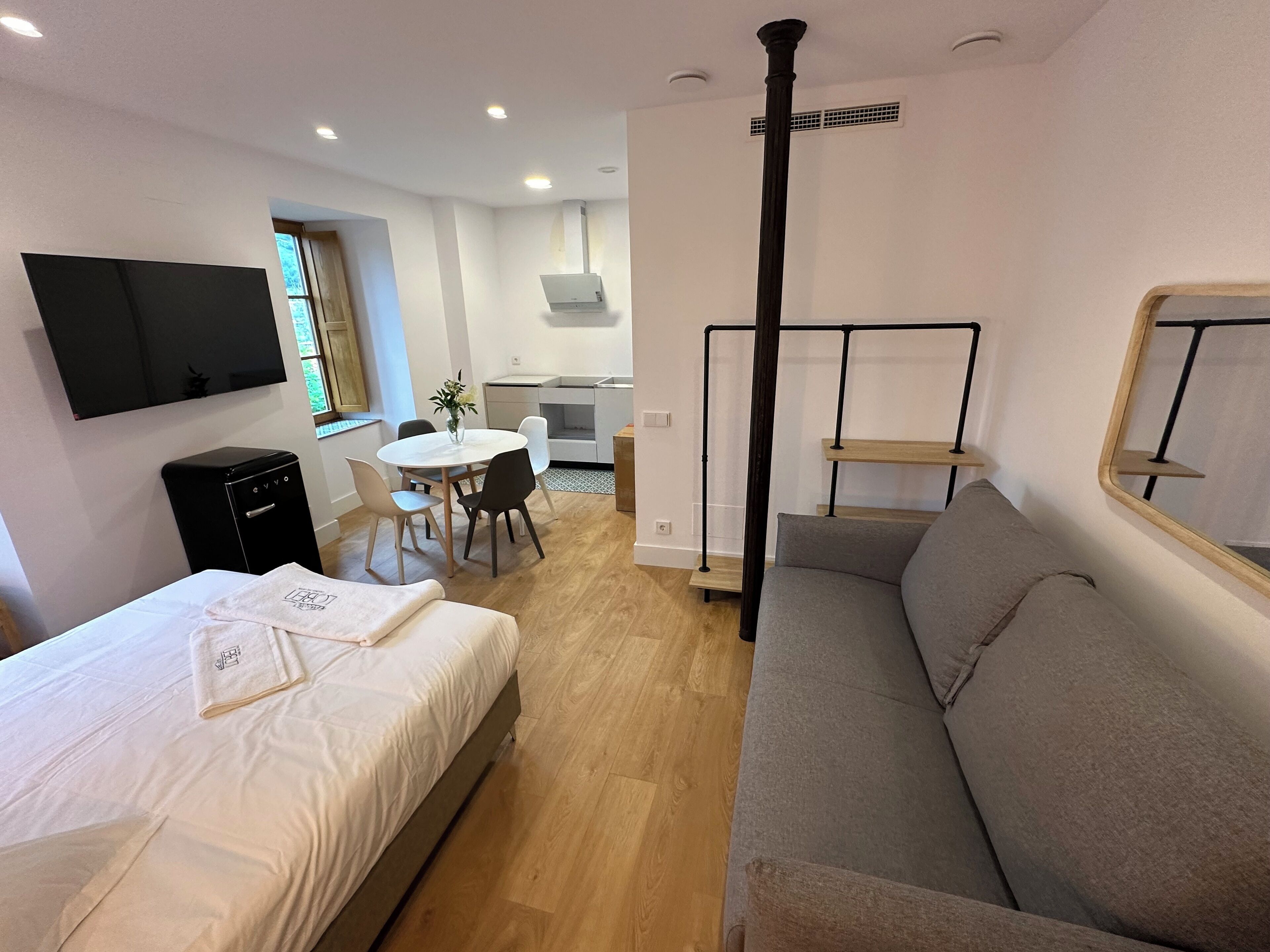 Ein modernes Hotelzimmer mit einem Bett, einem grauen Sofa, einem Fernseher, einem Schreibtisch und einem Essbereich.