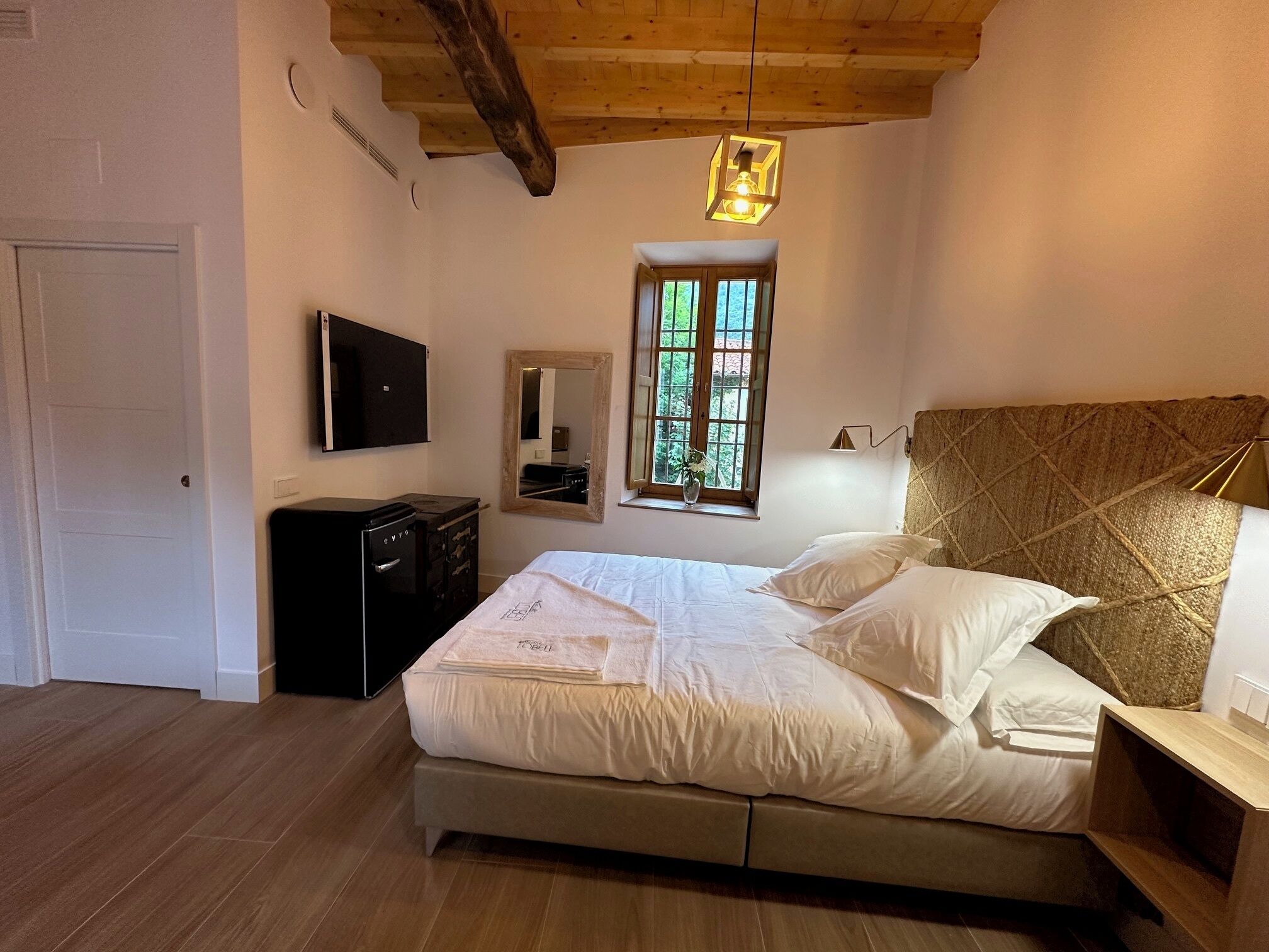 Un dormitorio con cama, televisor, cómoda, ventana y techo de madera.