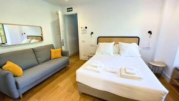 Une chambre d’hôtel avec un lit, un canapé gris agrémenté de coussins jaunes, un miroir et une porte portant l’inscription « SORTIE ».