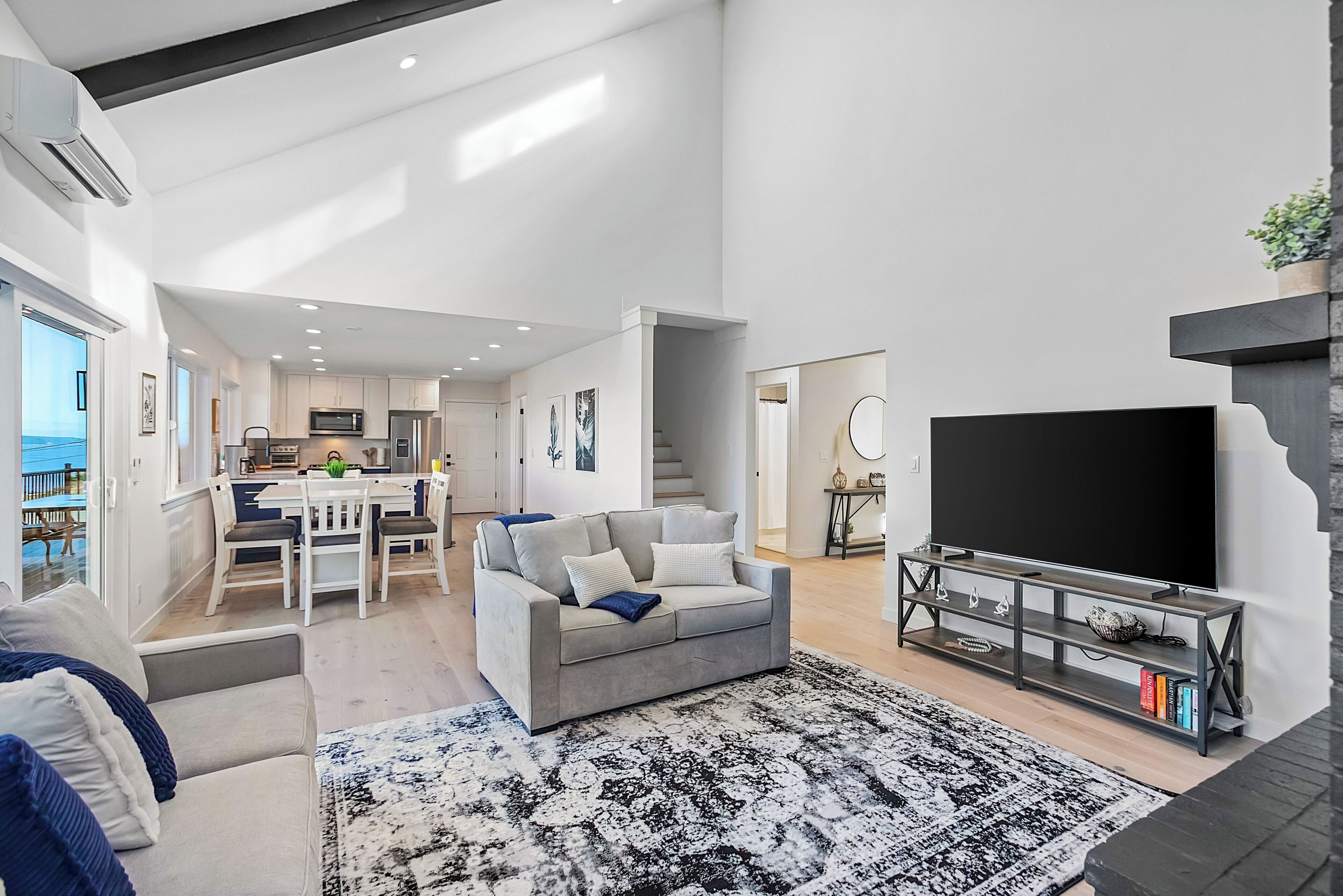Un salon moderne avec un canapé gris, un meuble TV noir et un tapis à motifs.