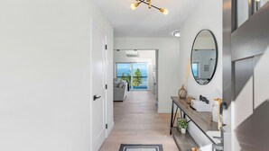 A modern hallway with a wooden floor, a black and white rug, a console table with decorative items, a large mirror, and a ceiling light fixture. - Peaceful Island Getaway Port Susan views (Camano Island)