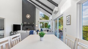 A modern living room with a white dining table, a fireplace, and a large window overlooking a balcony. - Peaceful Island Getaway Port Susan views (Camano Island)