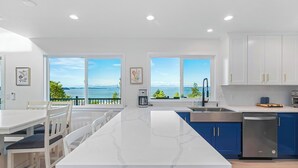 A modern kitchen with white cabinets, blue accents, a large island, and a view of the sea. - Peaceful Island Getaway Port Susan views (Camano Island)