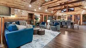 A spacious living area with a blue sofa, round coffee tables, and a dining area with chairs and a table. - 8-Bedroom Cabin with Indoor Pool, Private Mini Golf & Hot Tub Near Gatlinburg (Sevierville)